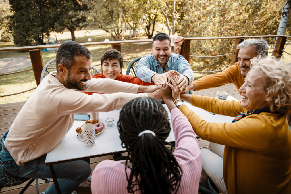 A group of people sitting at a table outdoors and doing a group high-five for their successful IOP drug and alcohol treatment