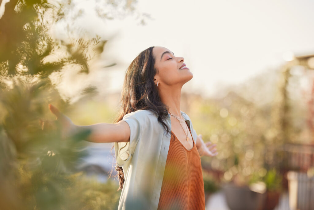 A woman lifts her arms and raises her head to soak in the sunlight and fresh air