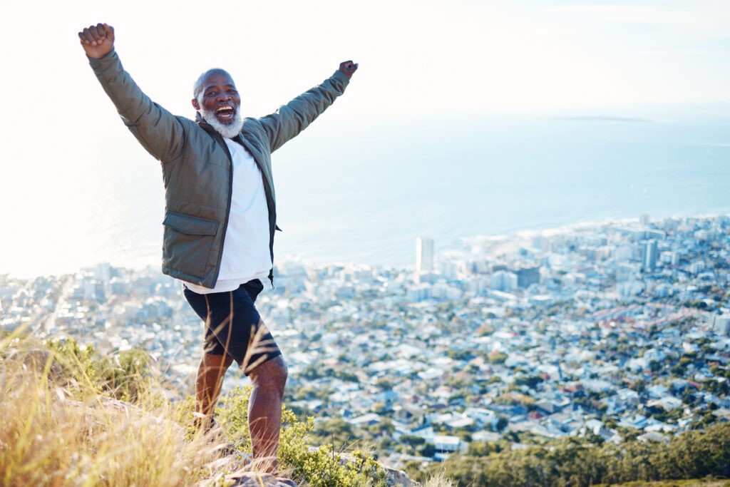 A man smiles and raises his arms in victory at the top of a hill overlooking the Los Angeles area