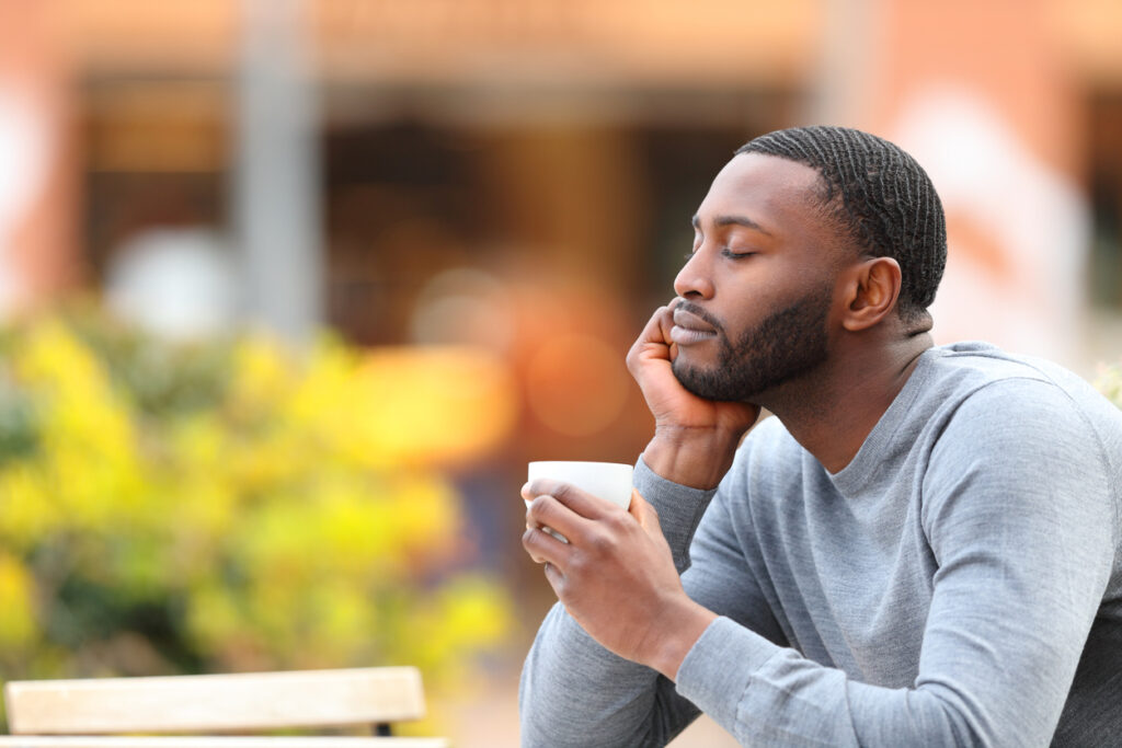 A young man enjoys the benefits of mindfulness for recovery as he sits at a café table outside, drinking an espresso