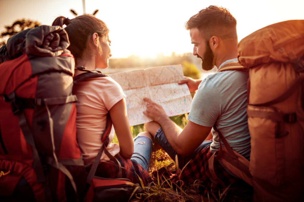 Two people with hiking backpacks sit next to each other and look over a map together