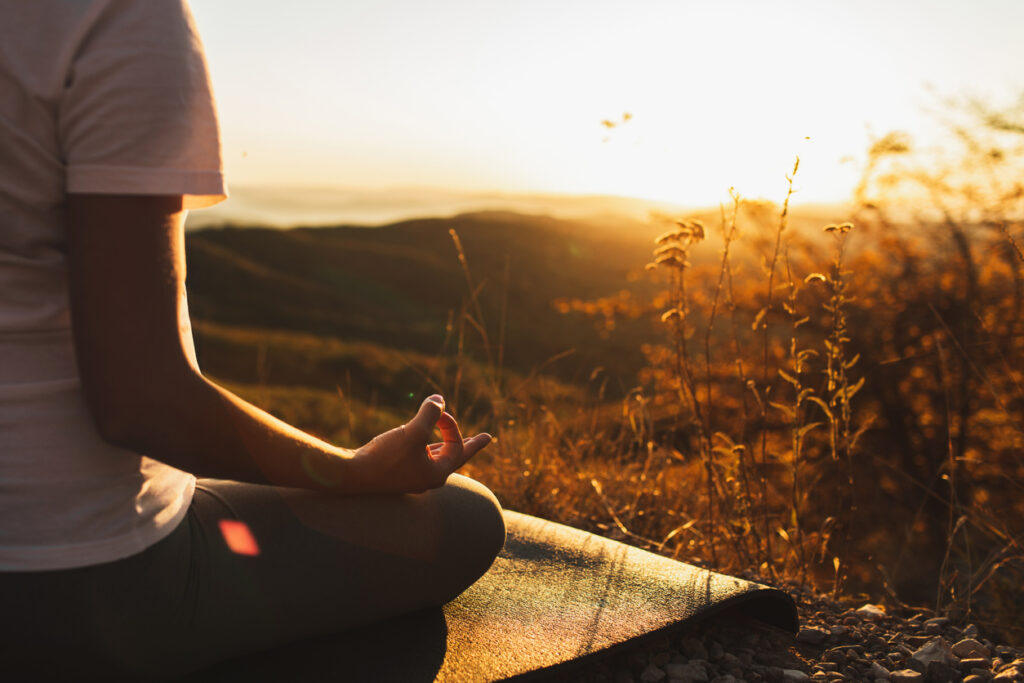 Someone practicing mindfulness meditation outside at the top of a hill during the sunset