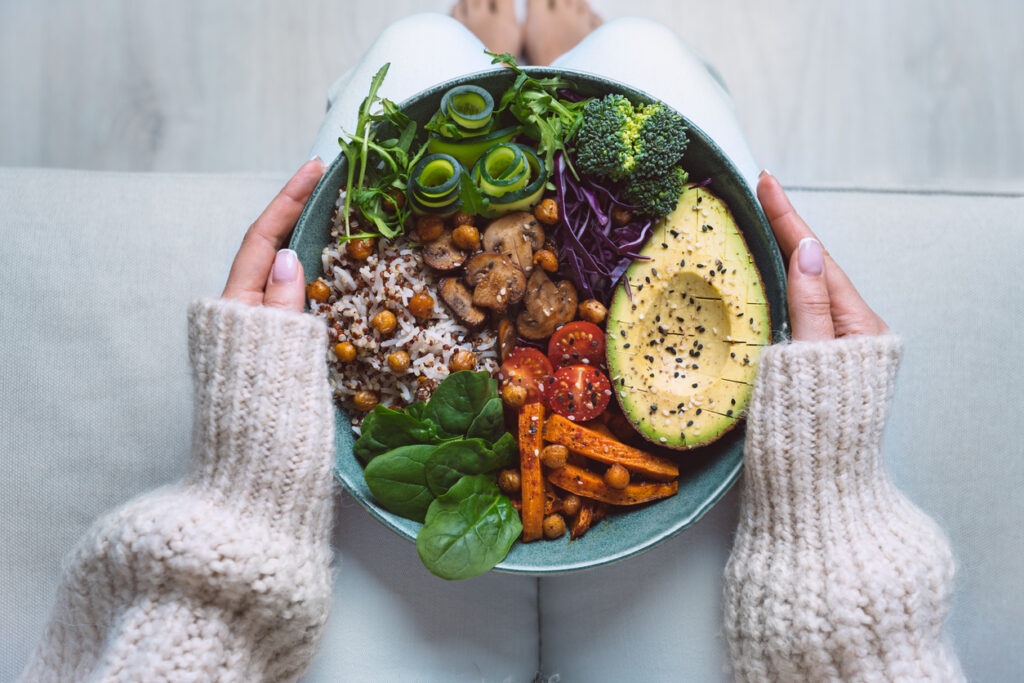 Someone holding a healthy and nutritious bowl of food including avocado, carrots, spinach, quinoa, broccoli, and mushrooms