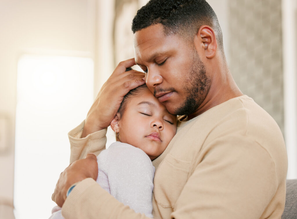 A father holding his sleeping child tenderly, focusing on his parenting after recovering from addiction