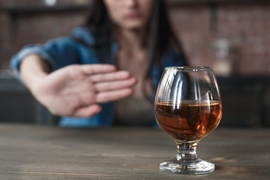 A woman sits at a table and holds her hand out to refuse a glass of alcohol on the table