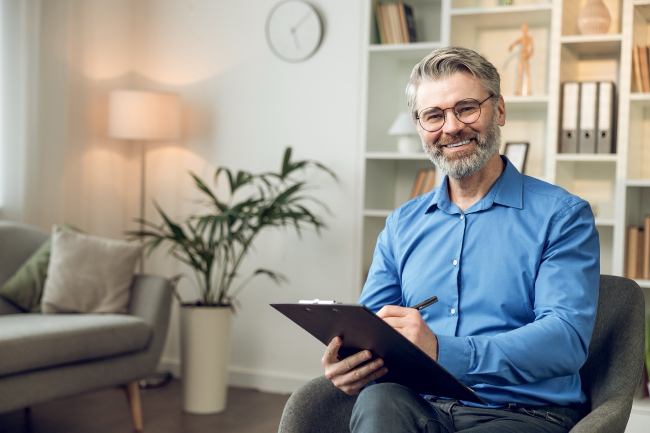 man,psychologist,wearing,blue,shirt,holding,clipboard,standing,in,his